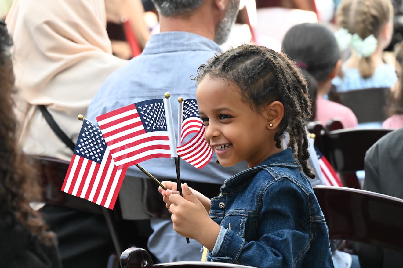 Seven-year-old Nael Welday from Angola waves three American flags at her dad at a citizenship ceremony that took place at the Children's Museum of Denver on Thursday, July 20.
