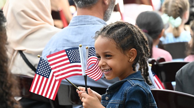 Nael Welday from Angola waves three American flags at a citizenship ceremony that took place at the Children's Museum of Denver on Thursday, July 20.