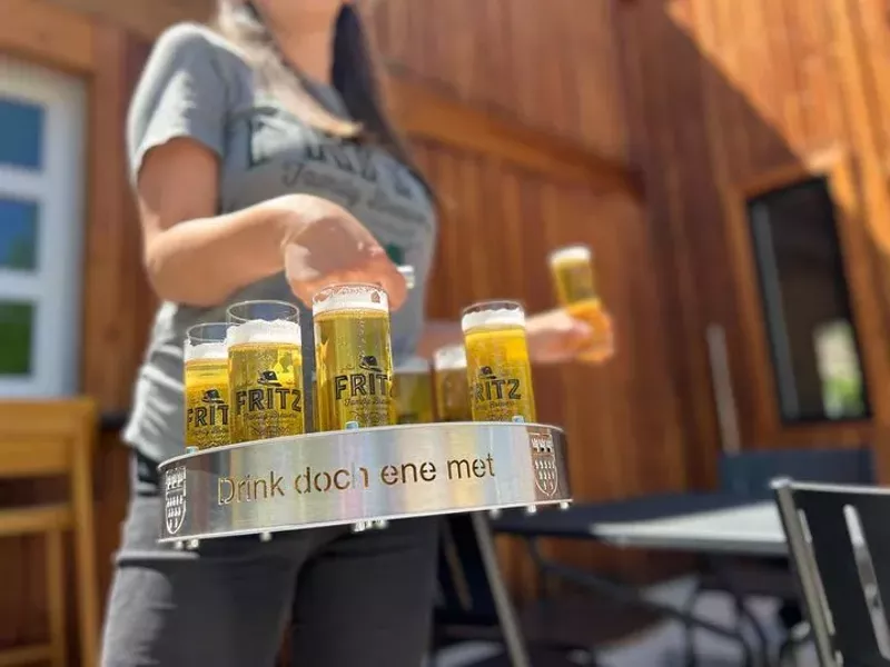 Image: a person carrying a metal tray of filled beer glasses
