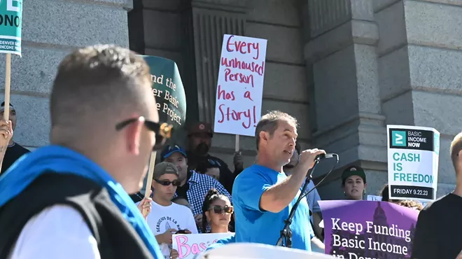 A man listens to another speak to a crowd.