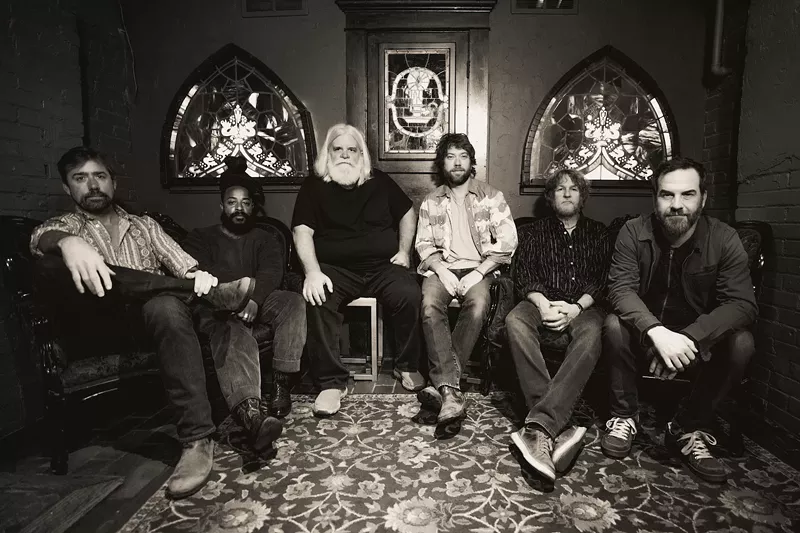 Image: six bandmates sit in a room