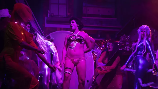 drag performers on stage with purple lighting.
