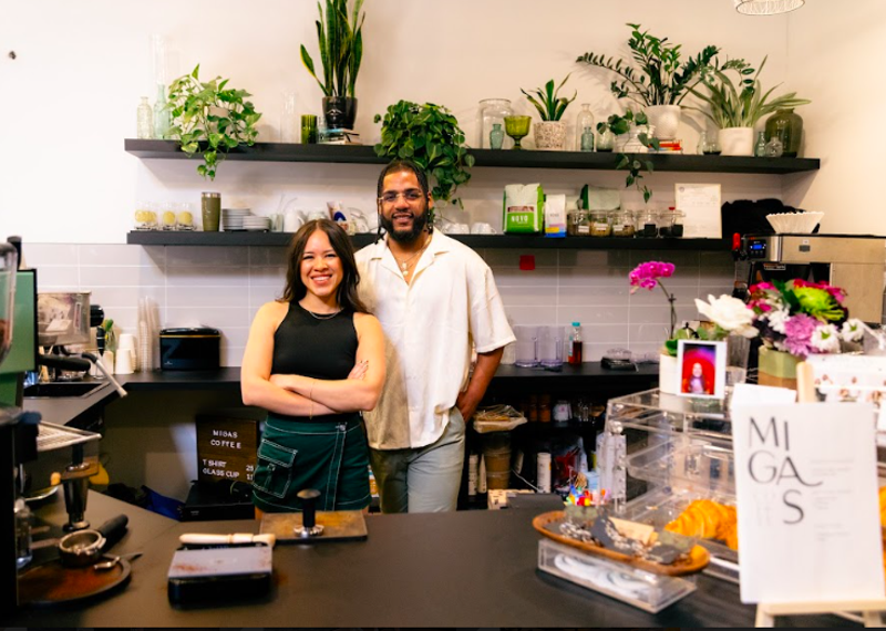 Image: a man and a woman posing behind a counter in front of plans on shelves