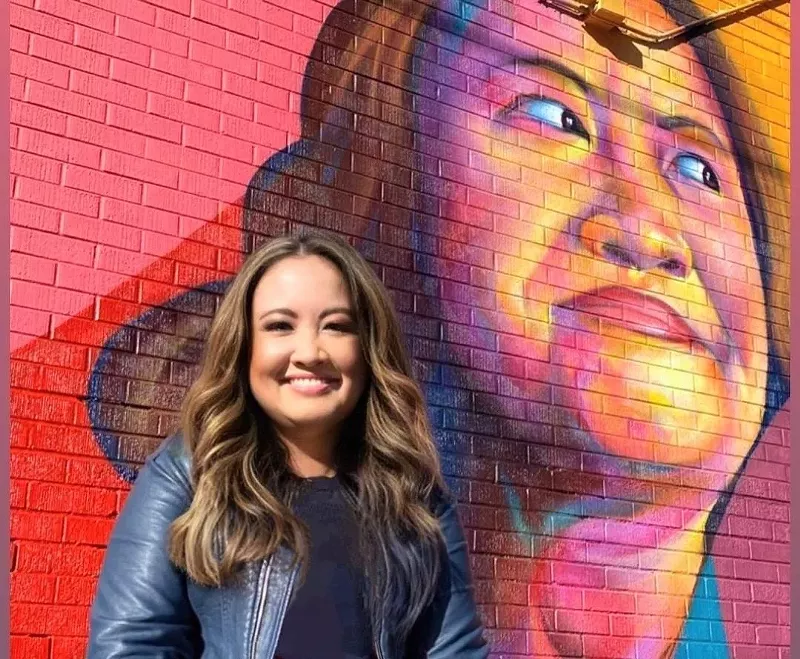 Image: Nga Vương-Sandoval in front of her portrait mural by I am Detour, aka Thomas Evans.