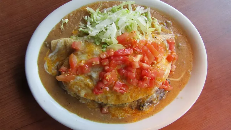 Image: green chile and cheese on top of a tortilla on a plate with lettuce and tomatoes