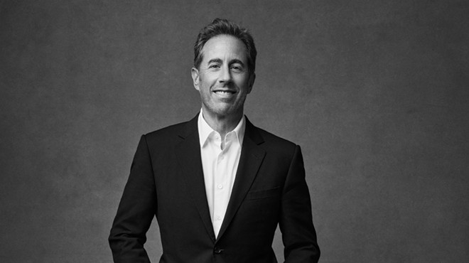jerry seinfeld poses in a black suit and white shirt