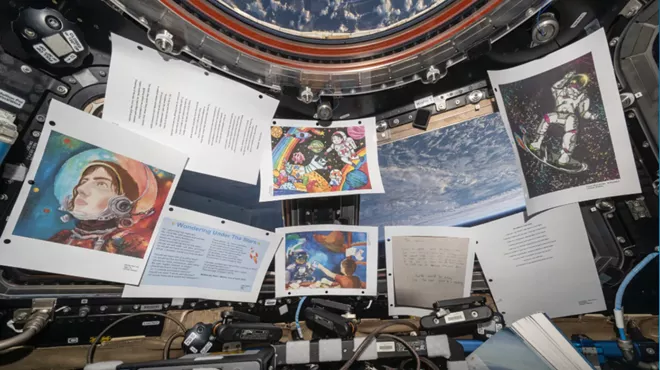 Printed out art hangs by a window looking out into the Earth's atmosphere