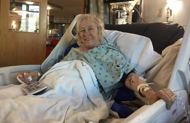 Image: A woman sits in a hospital bed.