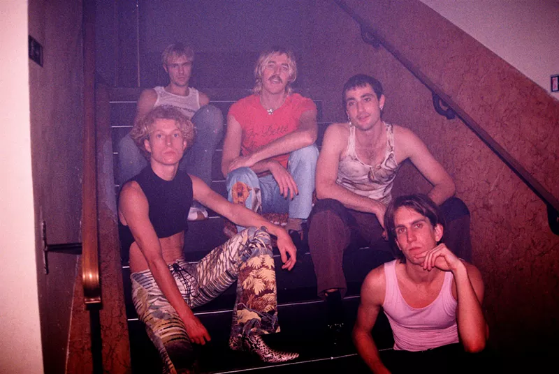 Image: a photograph of five men sitting in stairwell with pink lighting