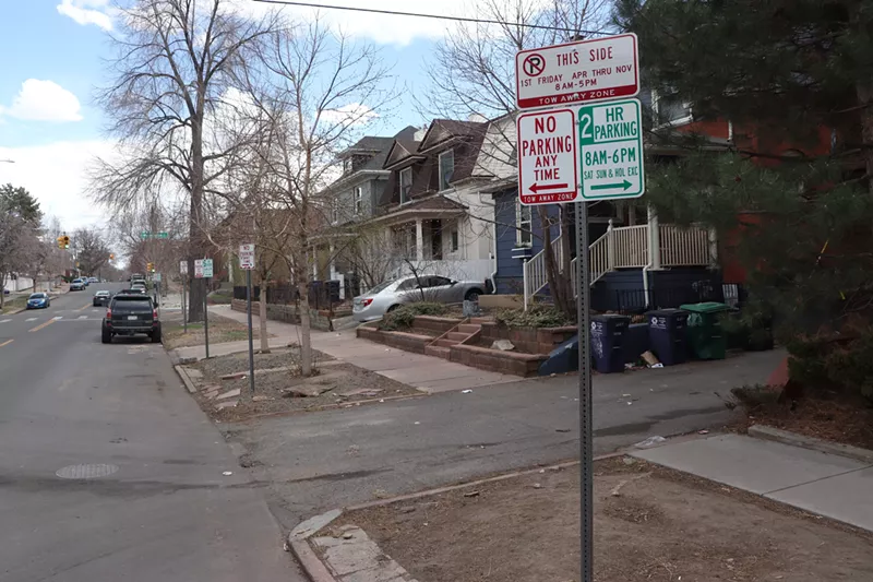 Image: A parking regulations sign graces the corner of a city street lined with single-family homes.