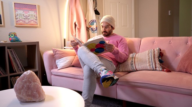 man in pink shirt reads book on pink sofa