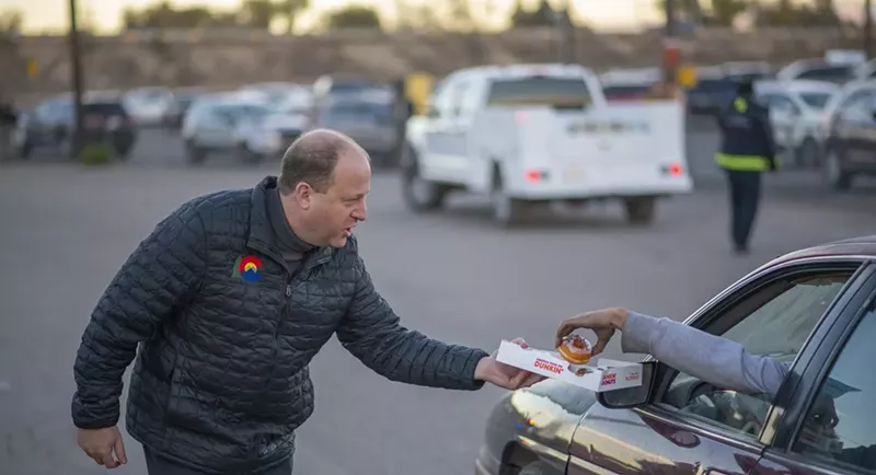 Image: Colorado Governor Jared Polis hands out free doughnuts to a driver