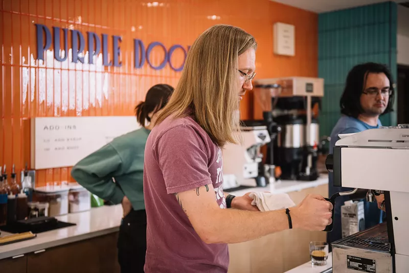 Image: a person making coffee behind a counter in a shop