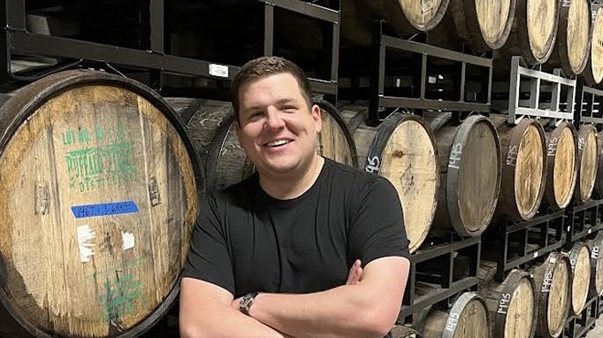 a man in a black t shirt stands in front of wooden barrels