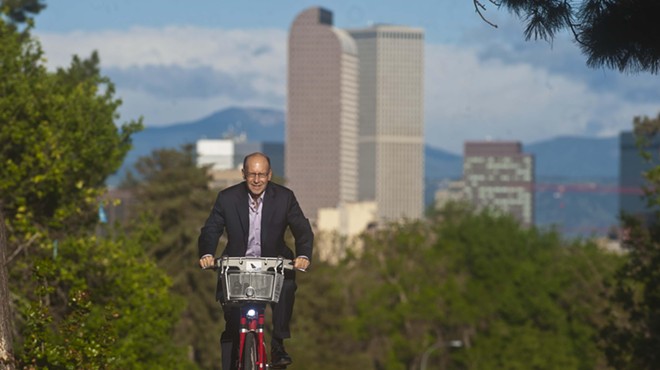 man on bicycle, denver skyline in background.