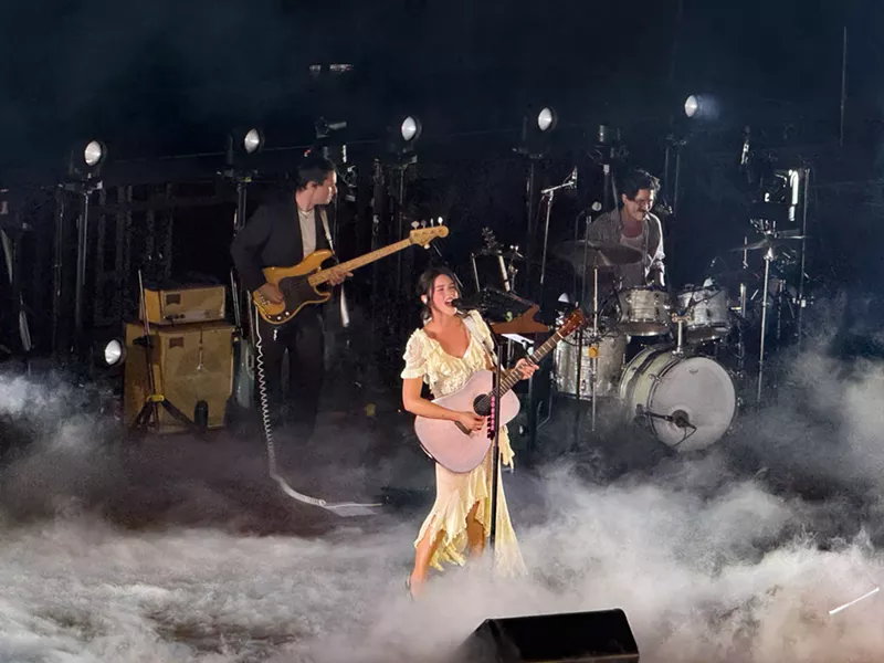 Image: Gracie Abrams performing with a guitar on stage with her band.