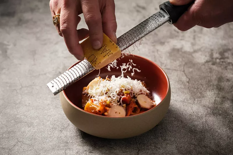 Image: a hand grating parmesan over a bowl of pasta