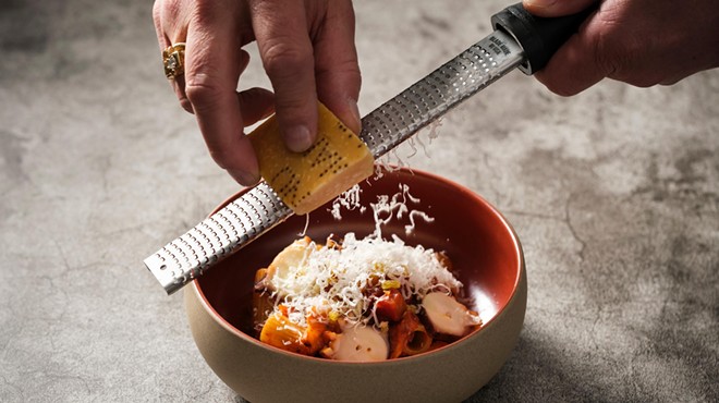 a hand grating parmesan over a bowl of pasta