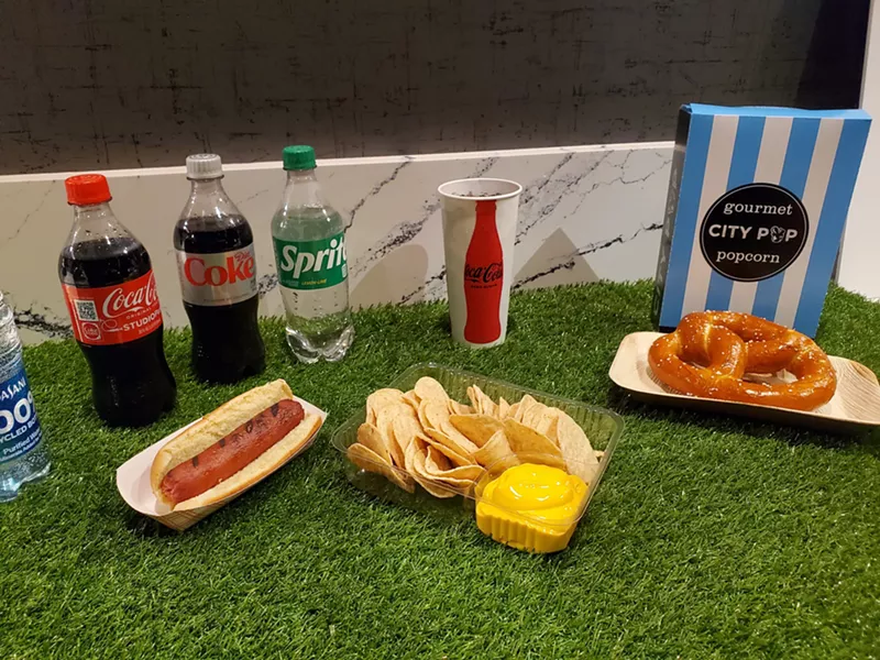 Image: bottles of soda, a hot dog, nachos, a bag of popcorn and a soft pretzel