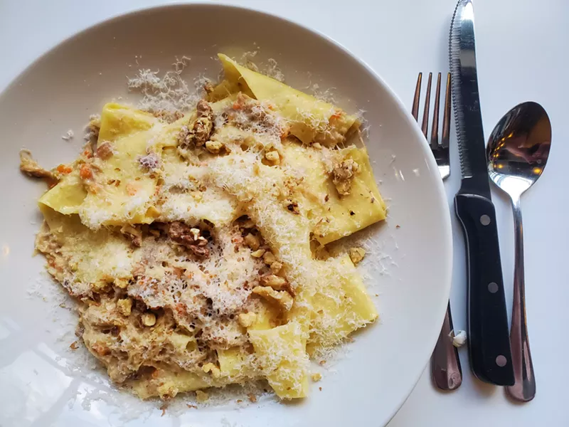 Image: a plate of pappardelle pasta nest to a fork and knife.