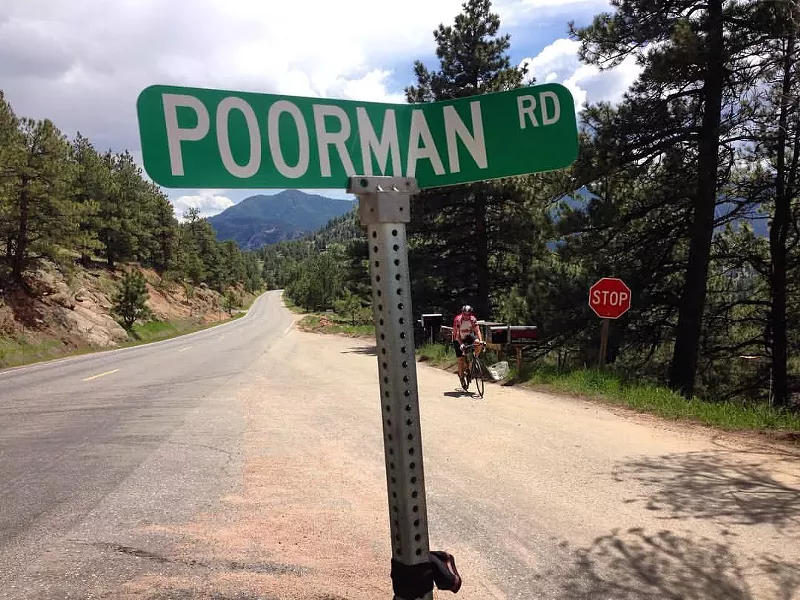 Image: A man rides a bike near a sign that reads Poorman