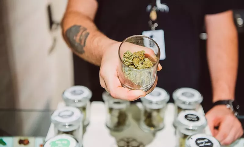 Image: A budtender displays jars of marijuana flower at a Colorado dispensary