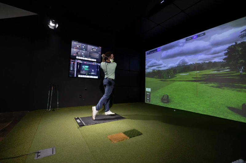 Image: Man swings golf clubs in indoor golf simulator