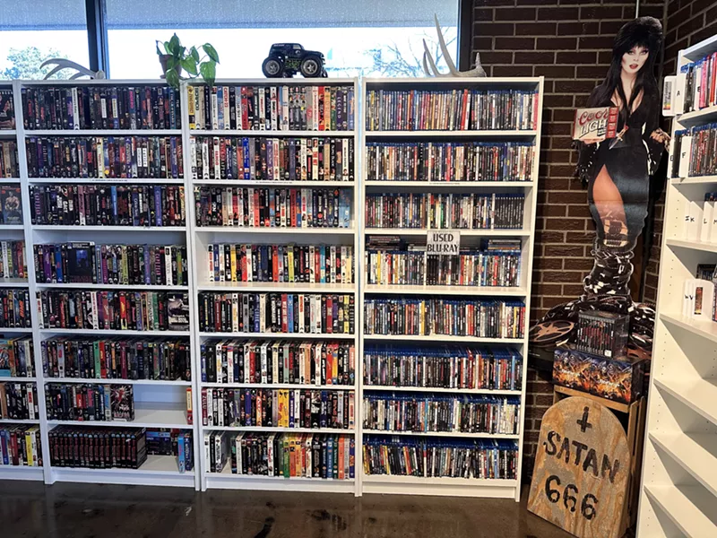Image: Elvira poses with VHS tapes at the Archive video store.