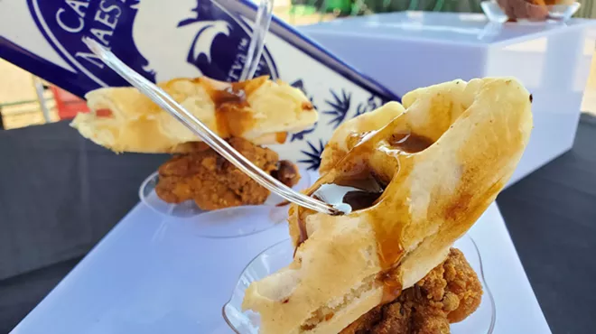 a piece of waffle over fried chicken with syrup