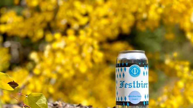 a can of beer on a log in front of trees with yellow leaves