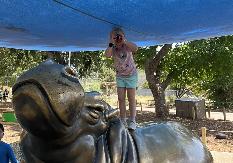 Image: A girl with binoculars stands on a hippo statue