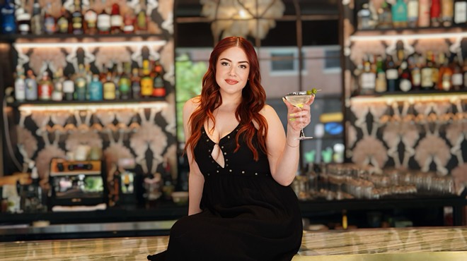 woman n a black dress sitting on a bar and holding a martini