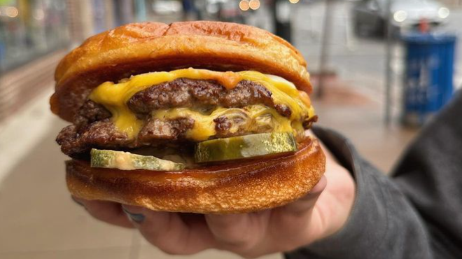 a hand holding a cheeseburger with pickles
