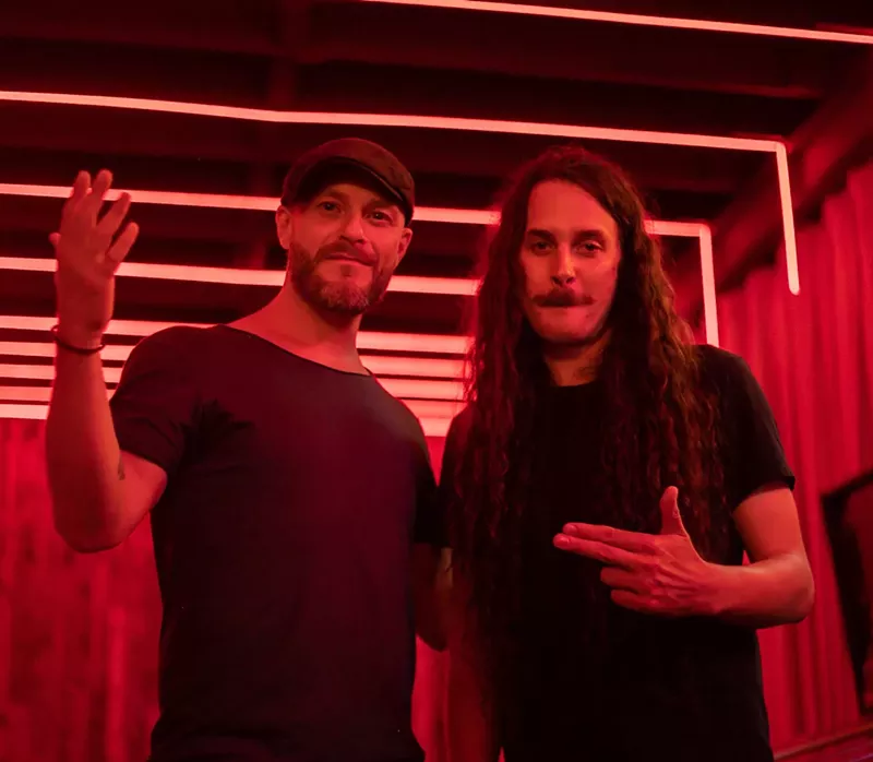 Image: Two men pose in a room with red lights.