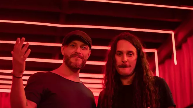 Two men pose in a room with red lights.