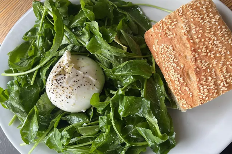 Image: A ball of cheese on greens with a side of bread.
