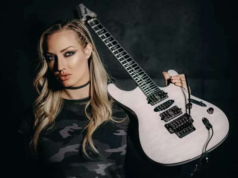 Image: woman resting a white electric guitar on her shoulder