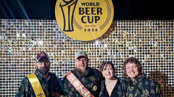 four people posing in front of a world beer cup sign