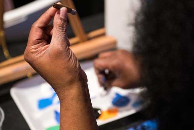 Hand holding a joint while person paints