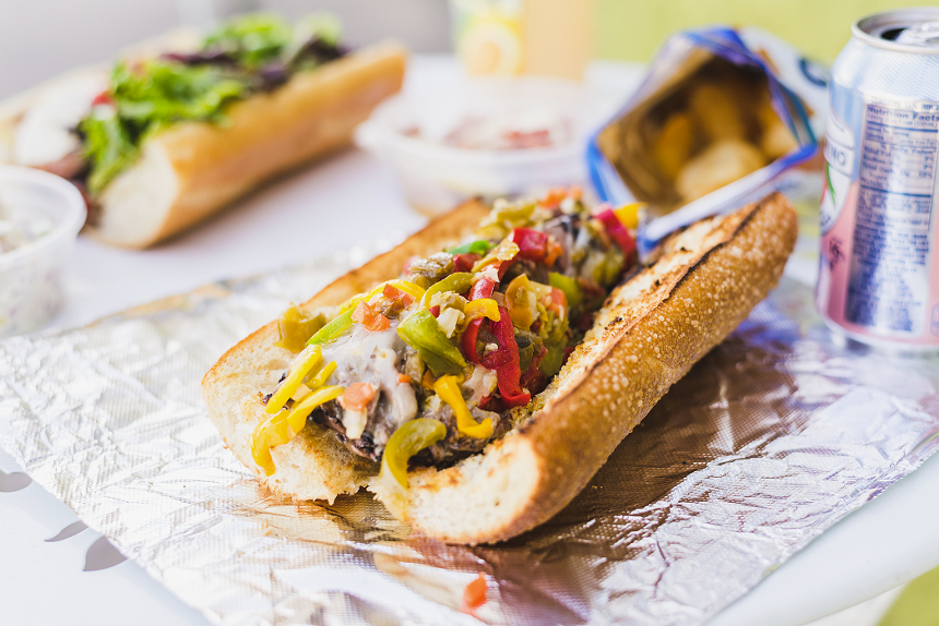 a beef sandwich on a long roll topped with red, green and yellow peppers
