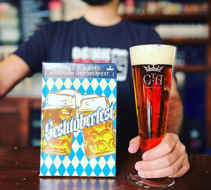 a man holding a tall glass of red beer next to a box of beer