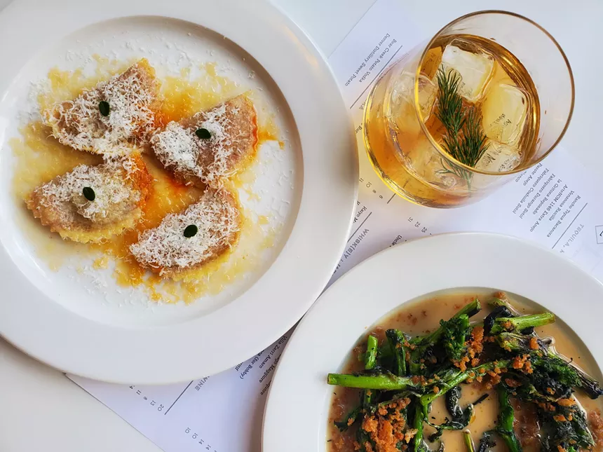 four mezzaluna on a plate next to a cocktail with dill and a plate of charred rapini.
