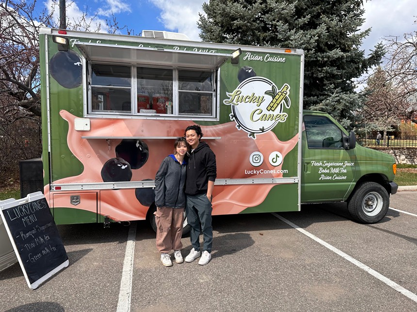 two people stand in from of a green and pink food trailer
