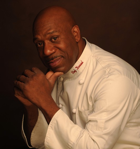 a man in a chef coat posing for a head shot