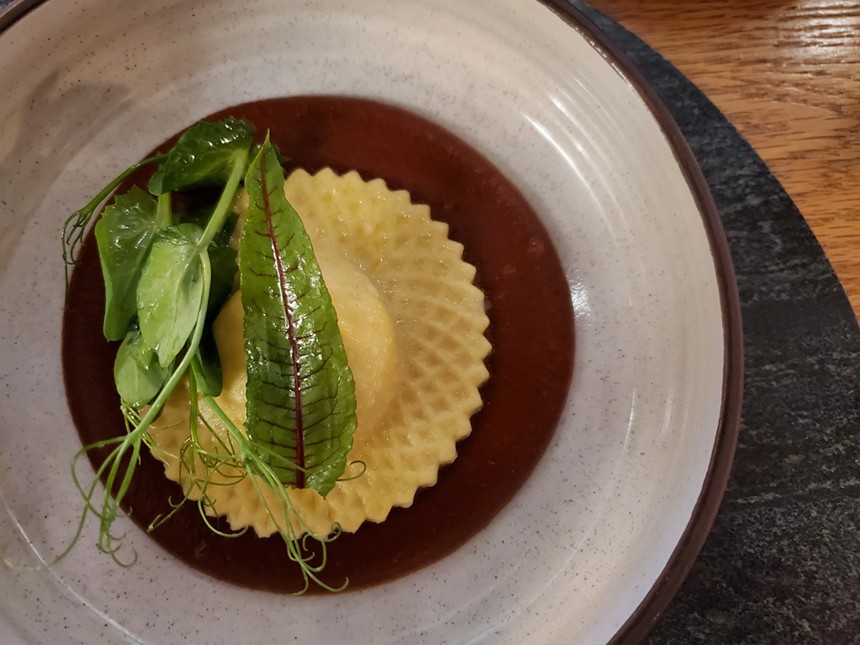 a large raviolo on a plate with greens on top