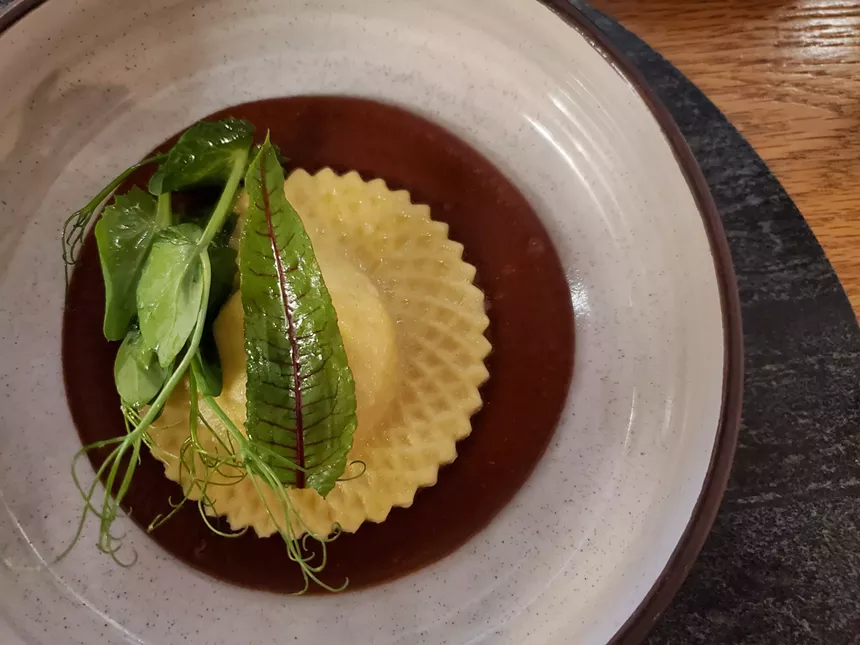 a large raviolo on a plate with greens on top