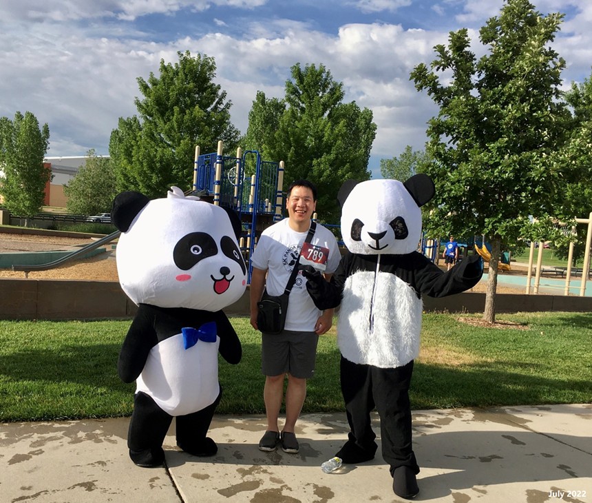 Man wearing a tag with the number "789" stands between two people in panda costumes.