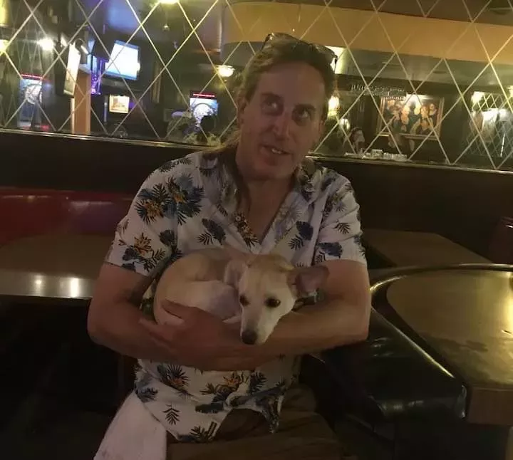a man in a tropical shirt holds a small white dog