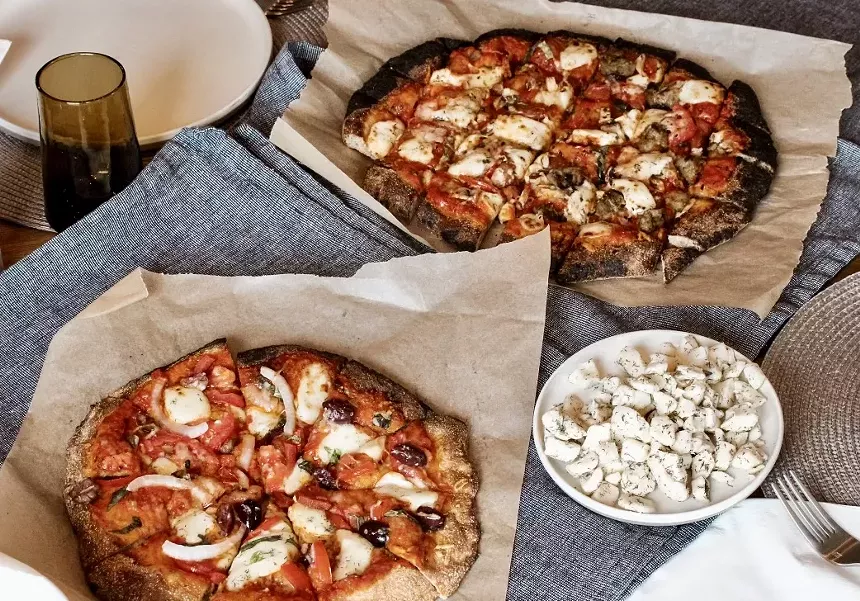 two pizzas on parchment paper and a plate of cheese curds