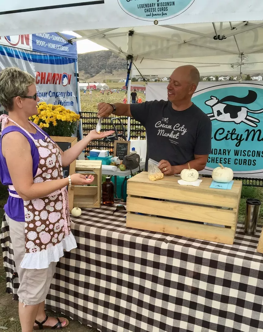 a man at a vendor tent handing cheese to a woman shopping